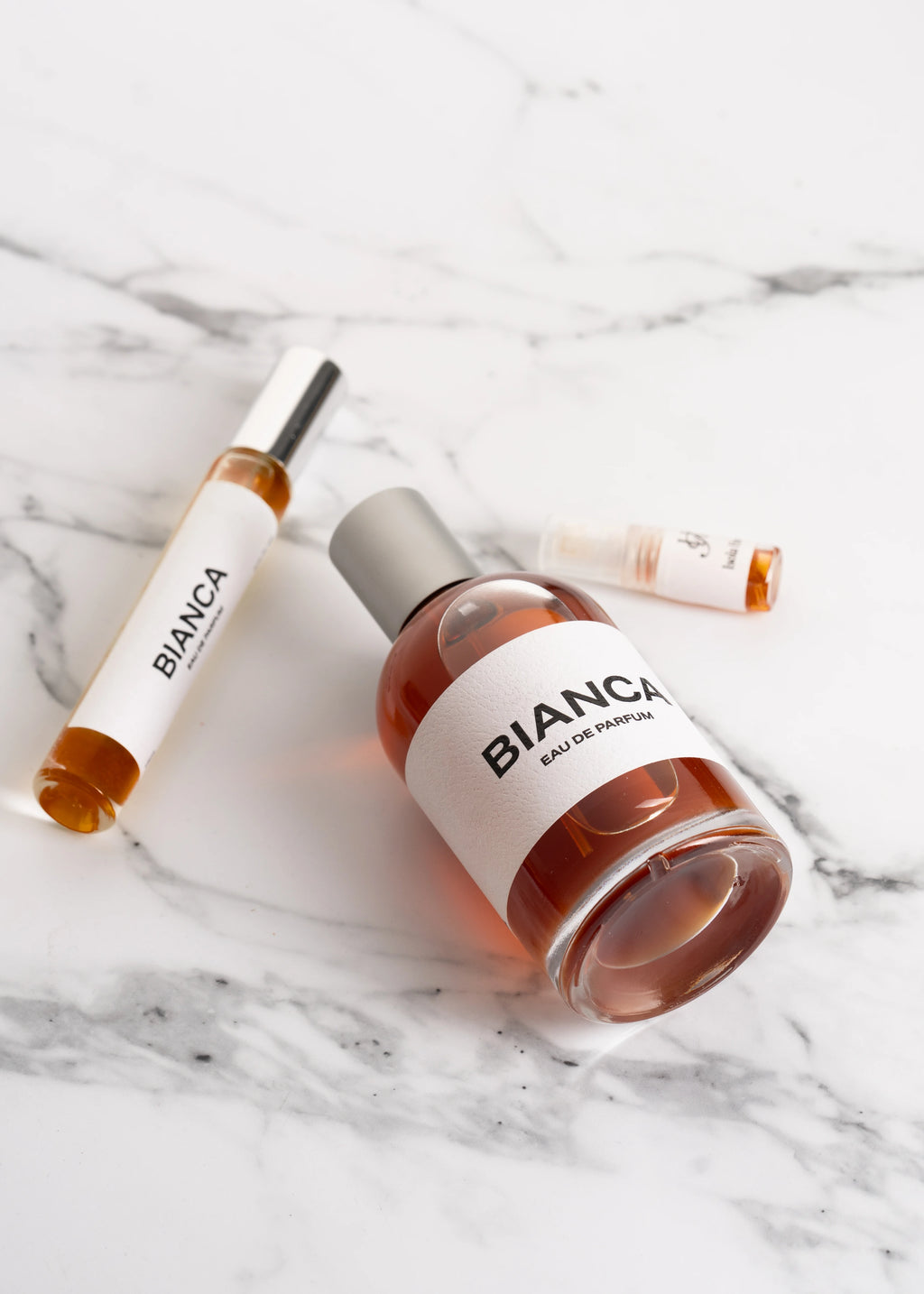 Three bottles of Bianca perfume on a marble surface